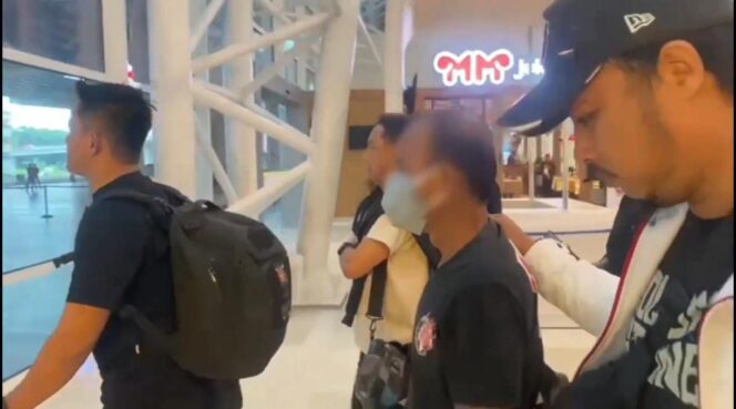 
					Andarias Tandung (pakai masker) saat tiba di Makassar, usai ditangkap tim gabungan di Sulawesi Utara. Foto: Istimewa